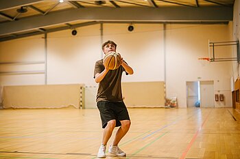 Ein junger Mann bereitet sich darauf vor, einen Basketball in einer Sporthalle zu werfen.