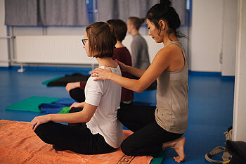 Yogalehrerin korrigiert bei einer Teilnehmerin die Haltung